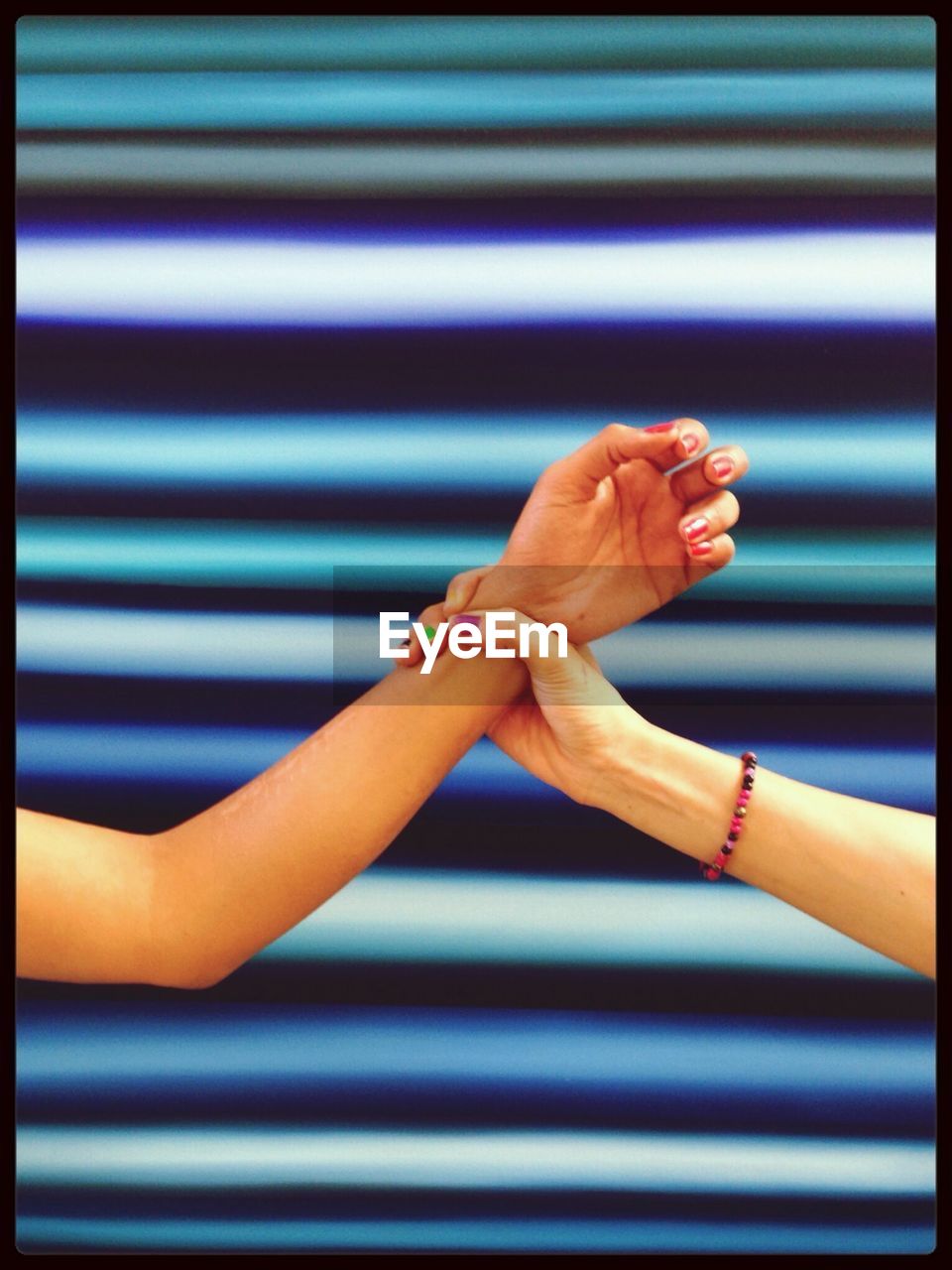 Cropped image of women holding hands against colored background