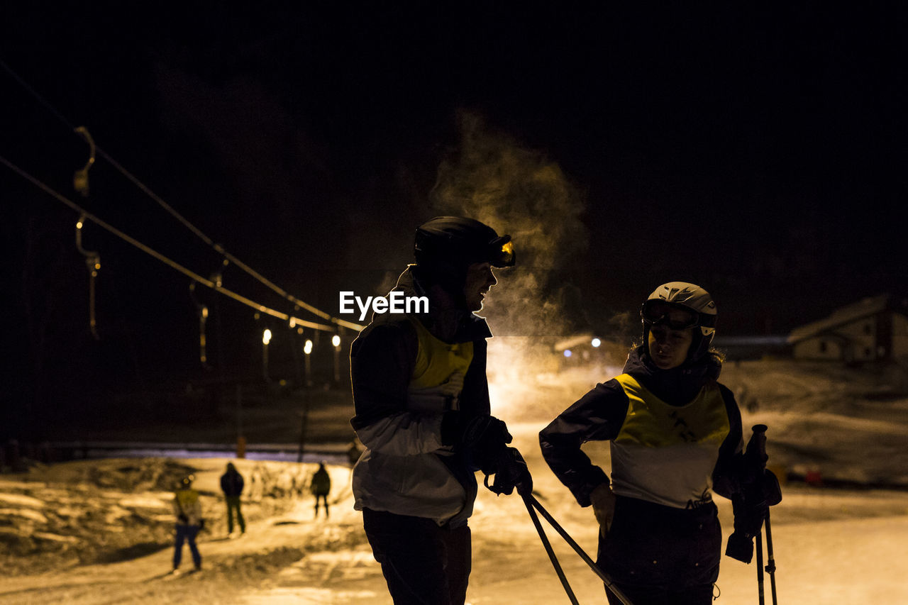 People standing on snow covered land against sky at night