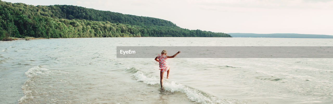 REAR VIEW OF WOMAN STANDING IN SEA