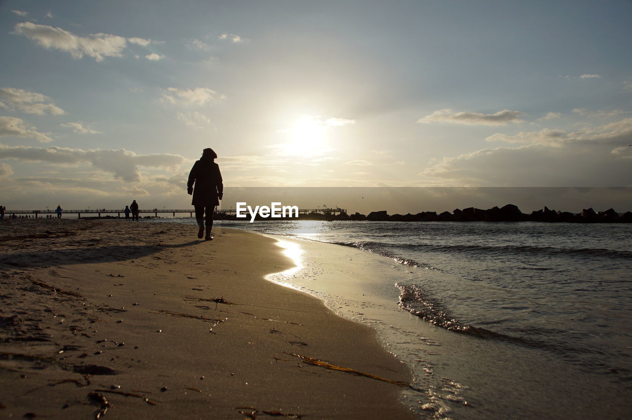 Rear view of silhouette man on beach against sky during sunset