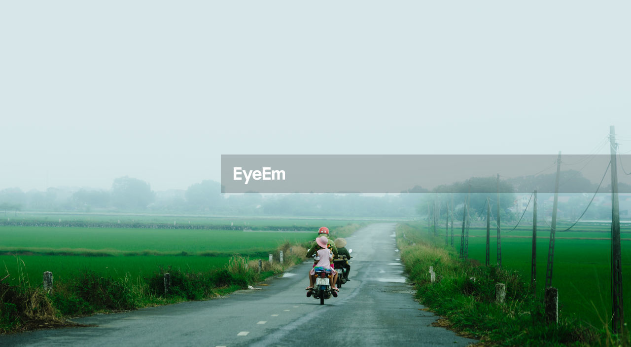 Rear view of people riding motorcycle on road against clear sky