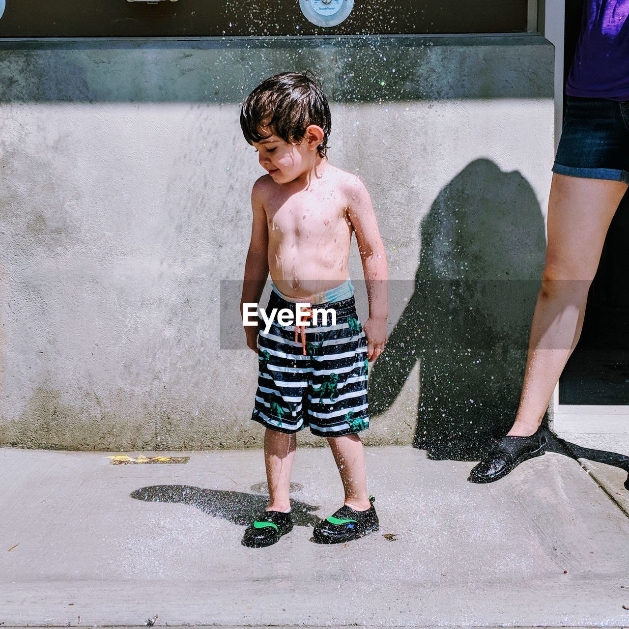 Water splashing on shirtless boy during sunny day