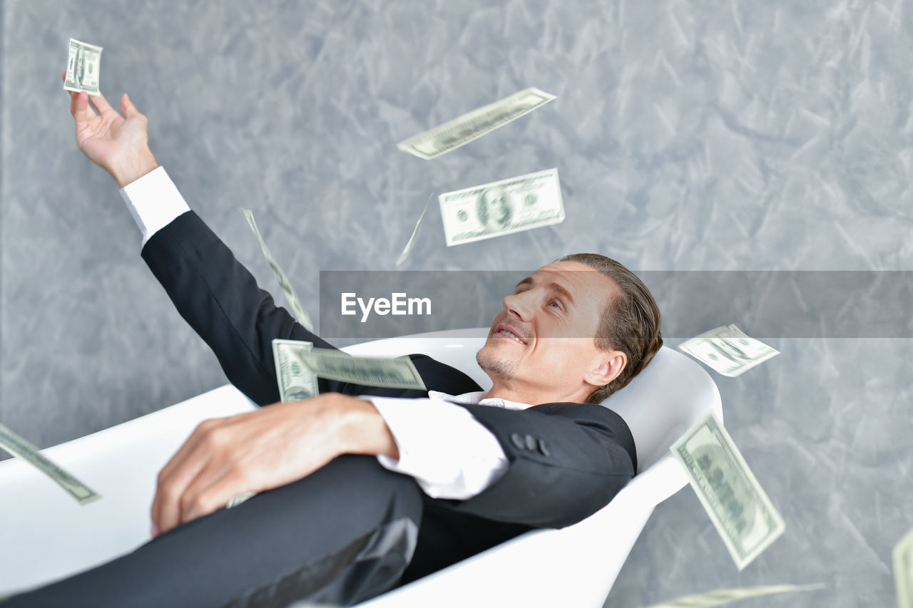 Businessman looking at paper currencies in mid-air while sitting on chair