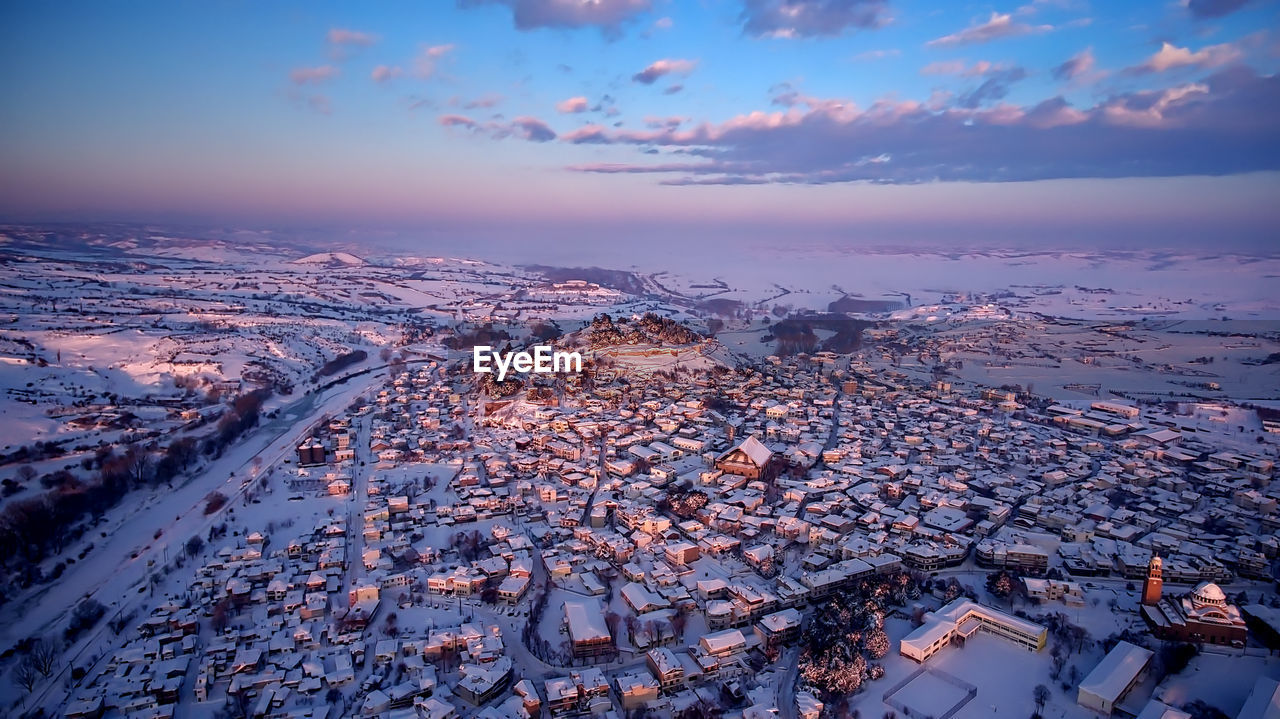 High angle view of snow covered townscape against sky during sunset