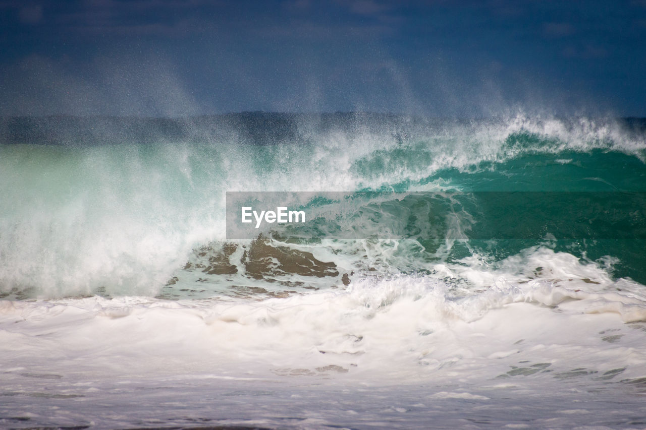 Waves rushing towards shore against sky