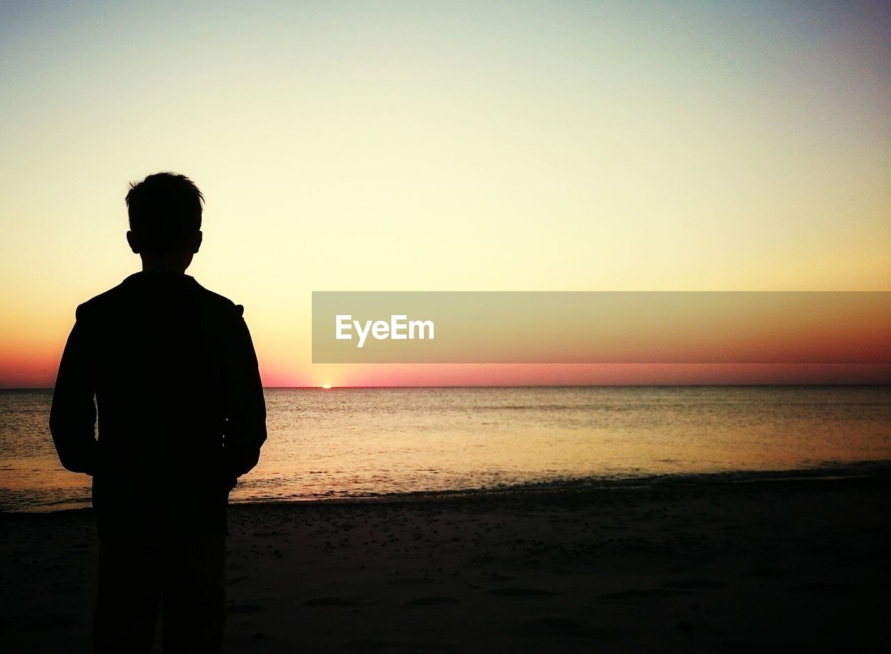 Rear view of silhouette man standing at beach against clear sky