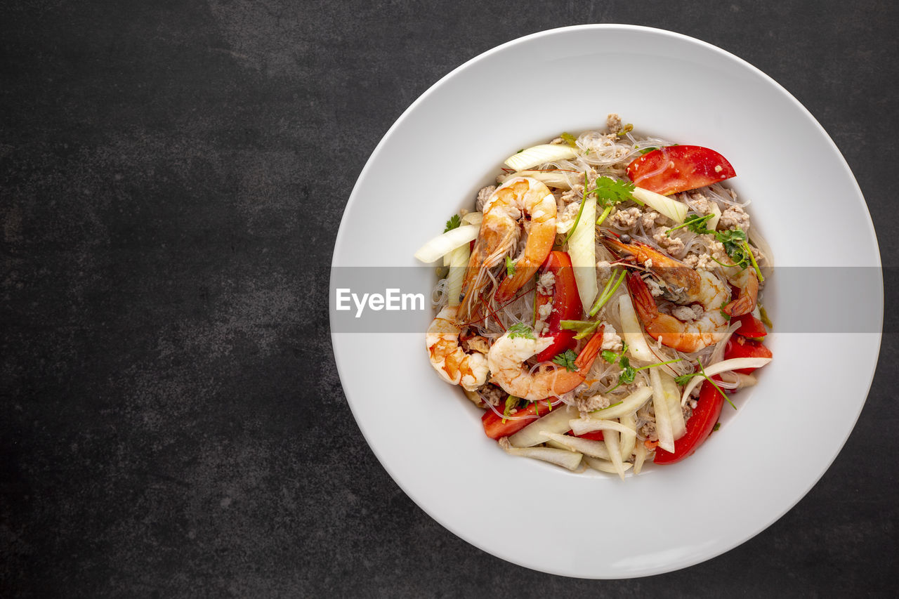 Yum woon sen, thai food, thai glass noodle salad in white ceramic plate on dark tone background