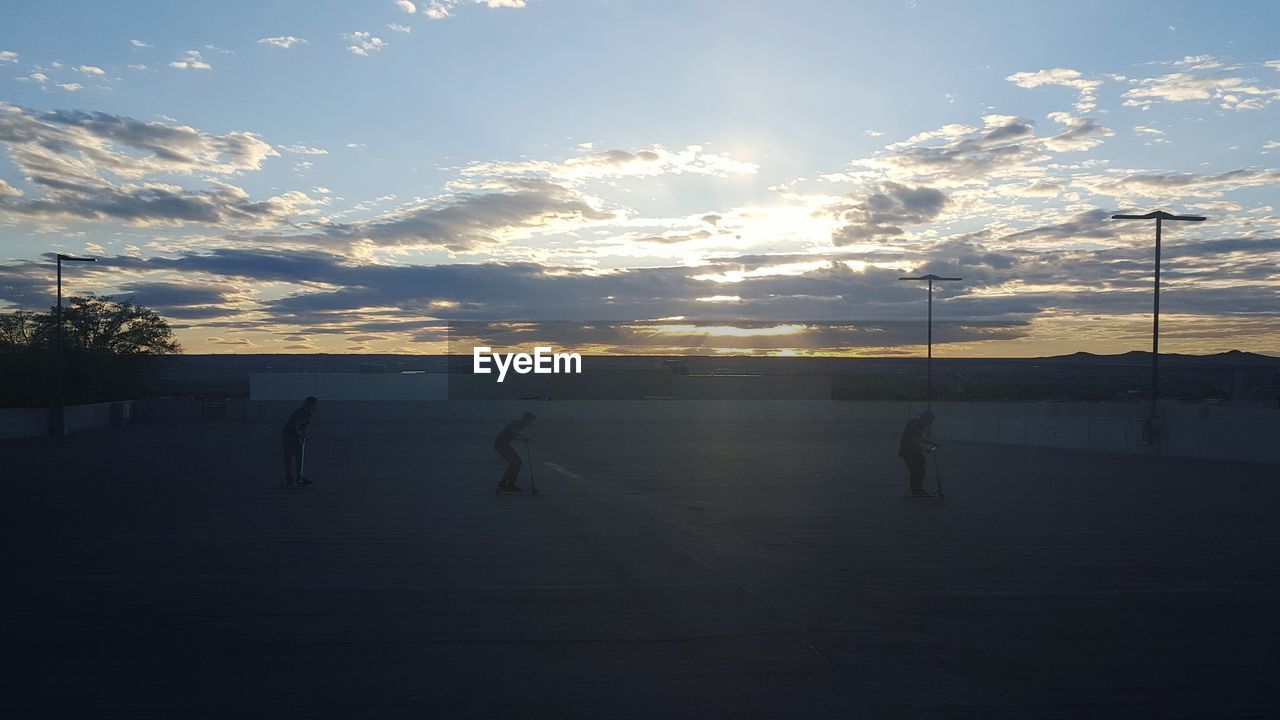 People with push scooters at parking lot against sky during sunset