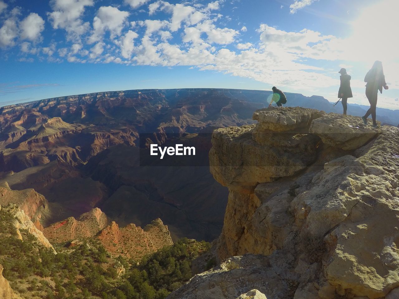 PEOPLE STANDING ON ROCK BY MOUNTAIN AGAINST SKY