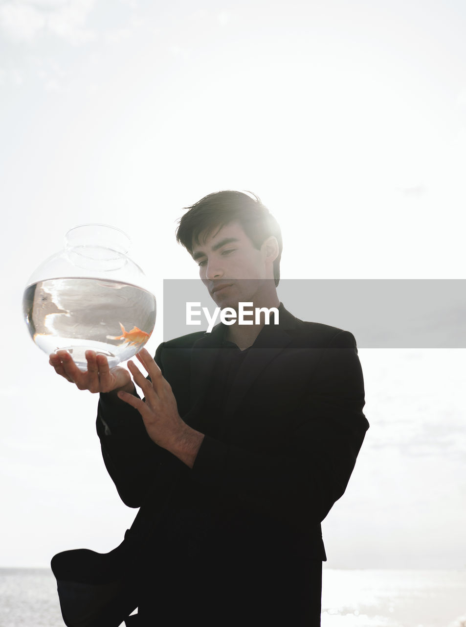 Young man holding fish tank against sky