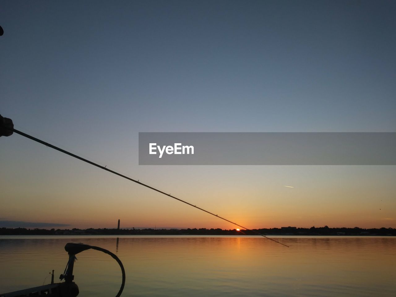 Silhouette fishing rod by sea against clear sky during sunset