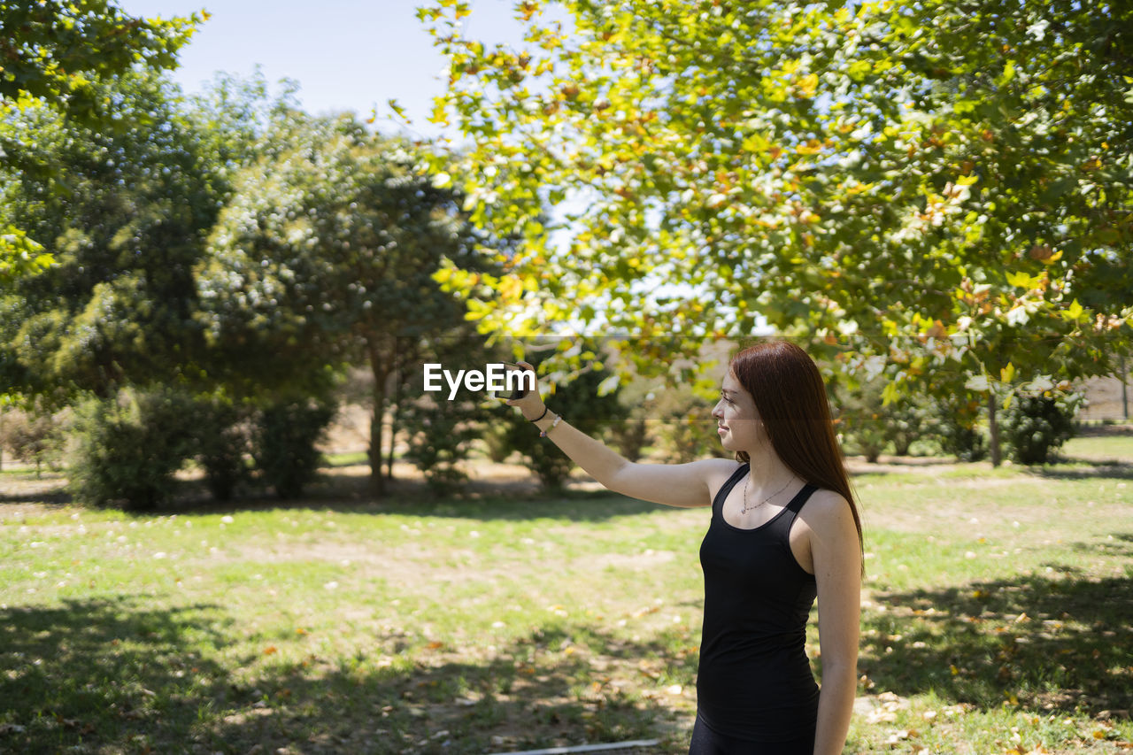 one person, plant, tree, women, nature, adult, hairstyle, young adult, long hair, sunlight, lifestyles, leisure activity, day, standing, autumn, three quarter length, outdoors, casual clothing, tranquility, green, rear view, growth, beauty in nature, relaxation, leaf, flower, clothing, person, brown hair, park, looking, grass, female, park - man made space, dress, lawn, shadow, contemplation, fashion, waist up, wellbeing, garden