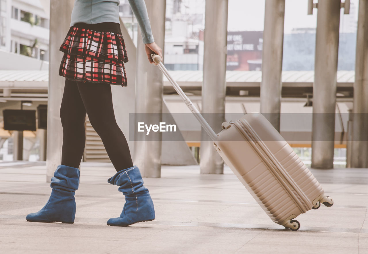 Low section of woman with suitcase walking on floor