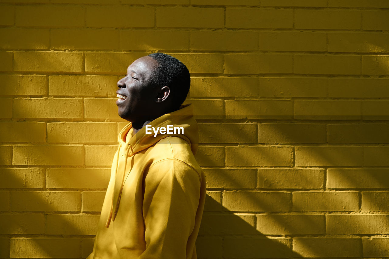 Side view of cheerful man standing against wall