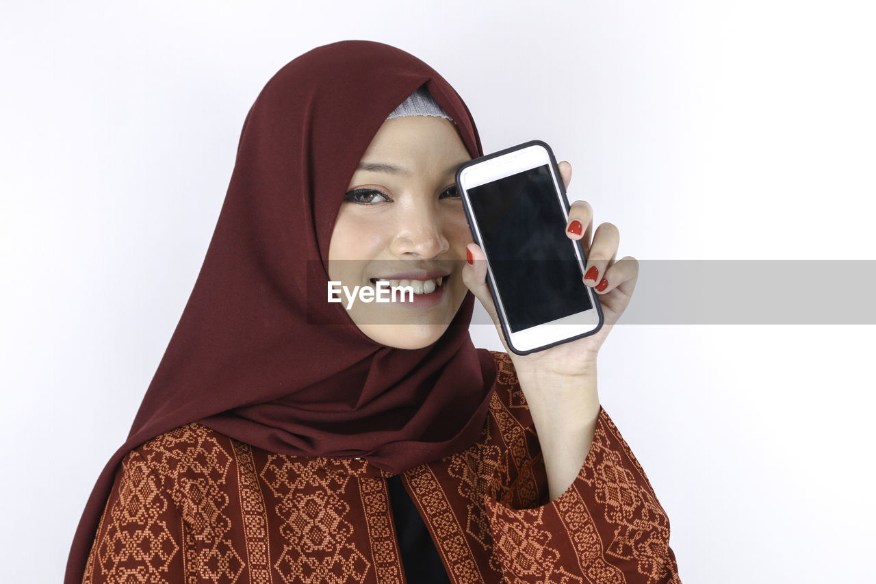 PORTRAIT OF SMILING YOUNG WOMAN USING SMART PHONE