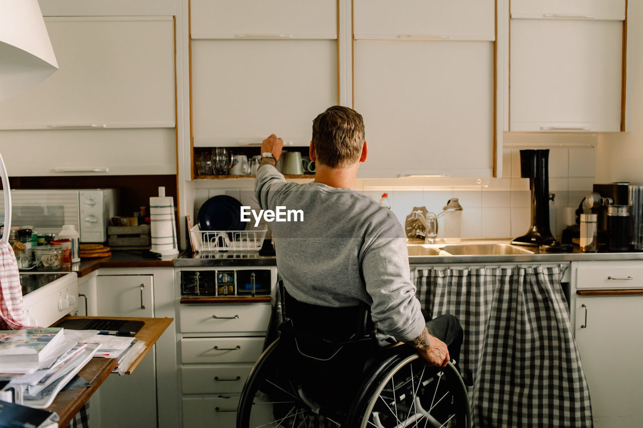 Rear view of disabled man opening cabinet in kitchen at home