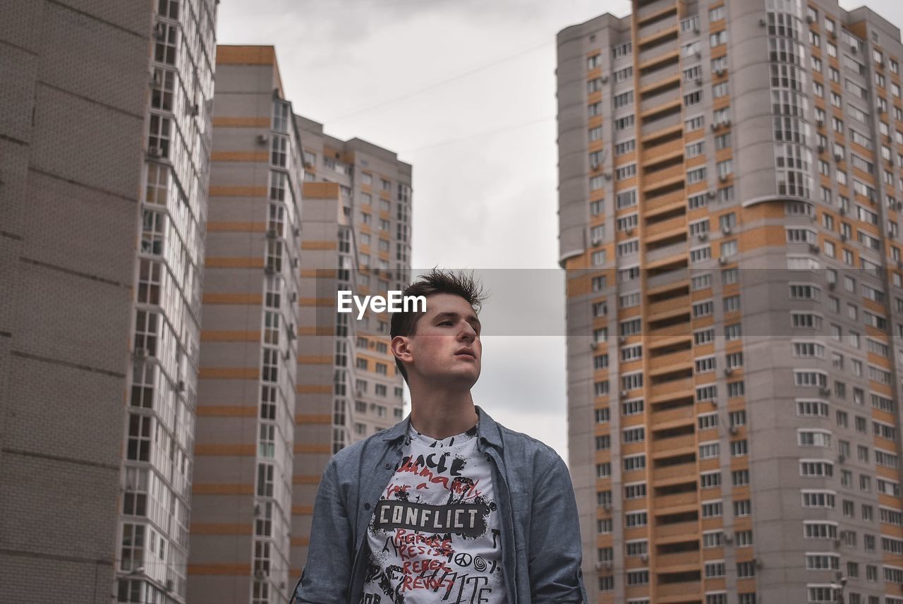 Low angle view of young man looking away against buildings in city