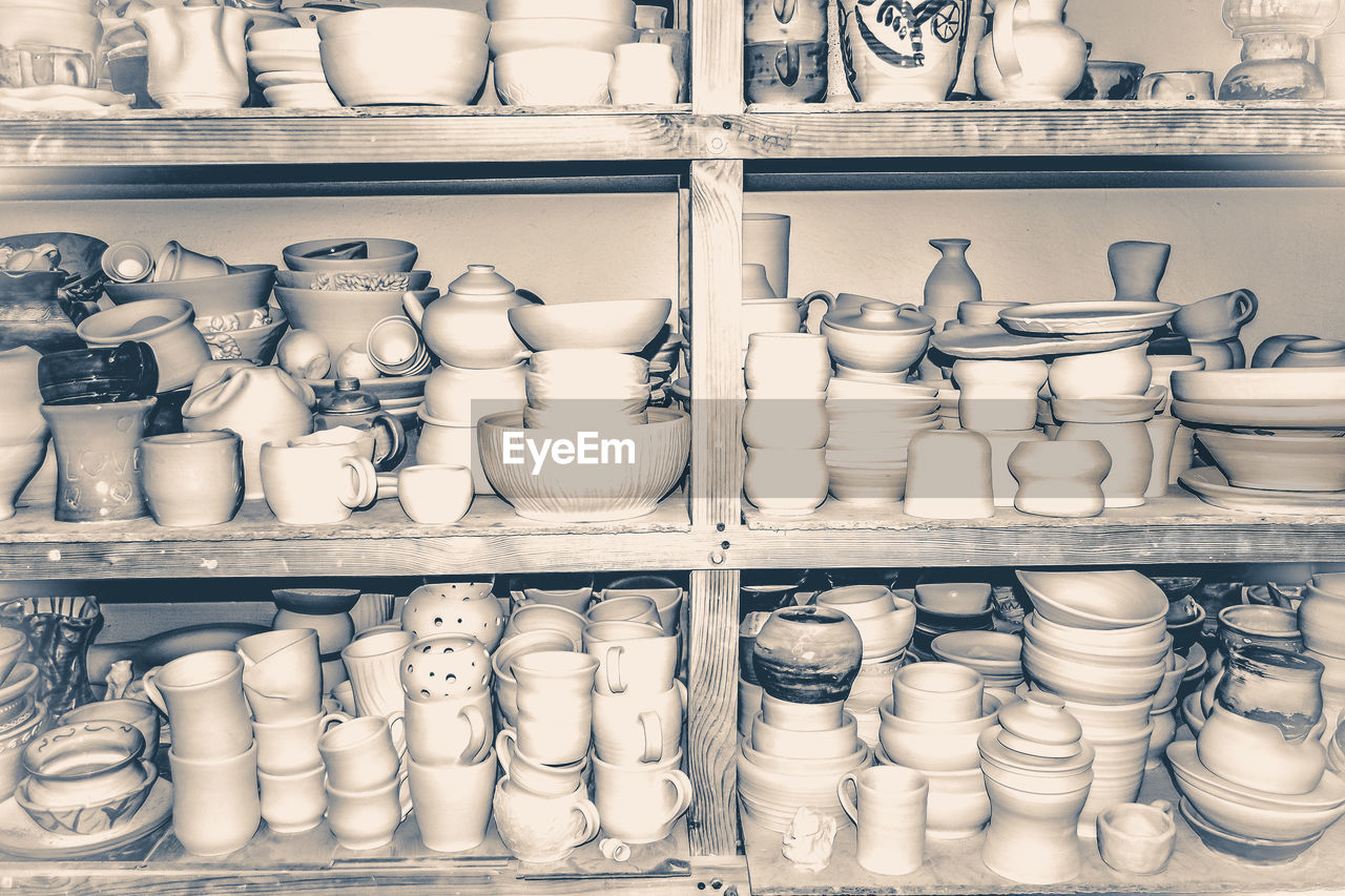 Bright pottery. many white, not painted clay pottery standing on wooden shelves