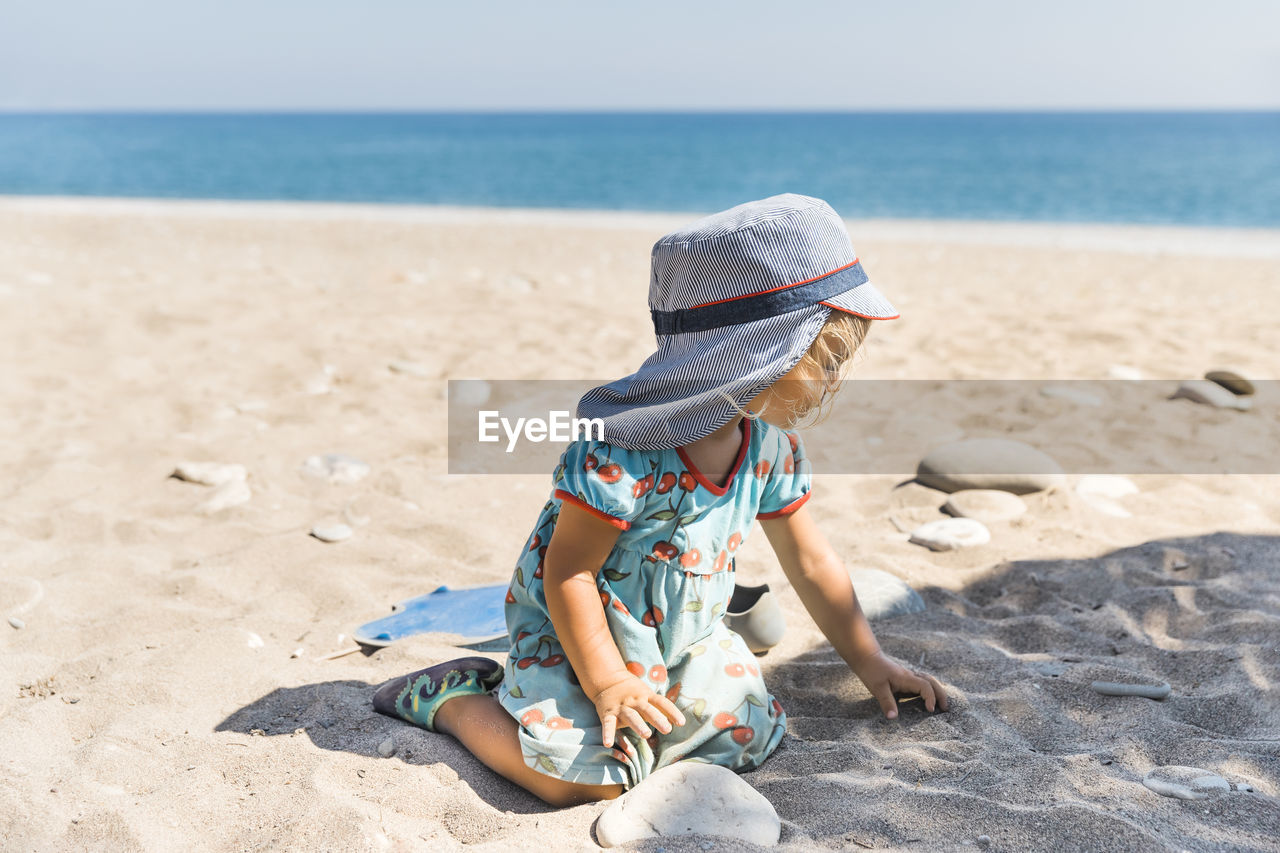 BOY WEARING HAT ON BEACH AGAINST SEA