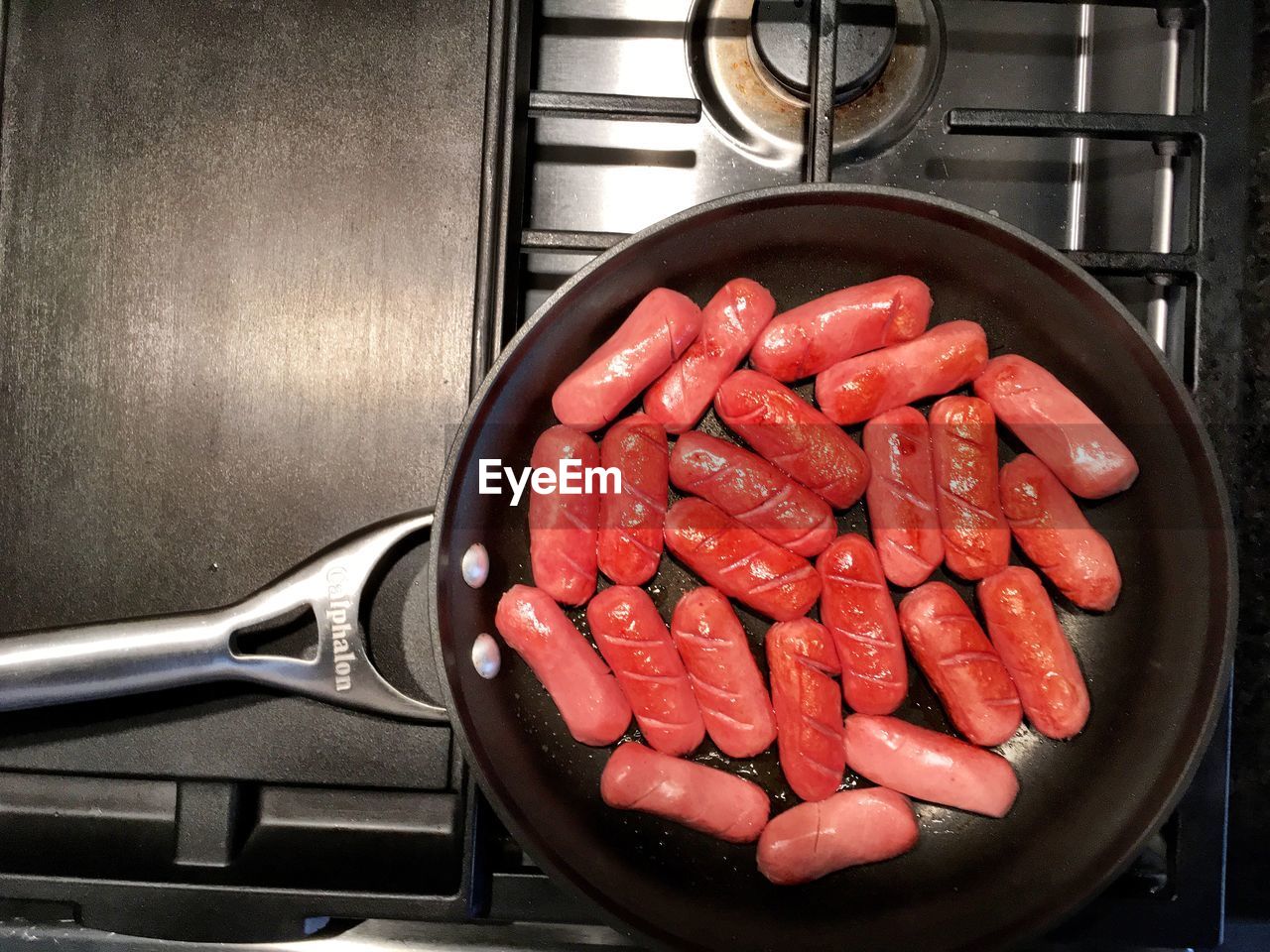 Directly above shot of sausages cooking in pan on gas stove burner