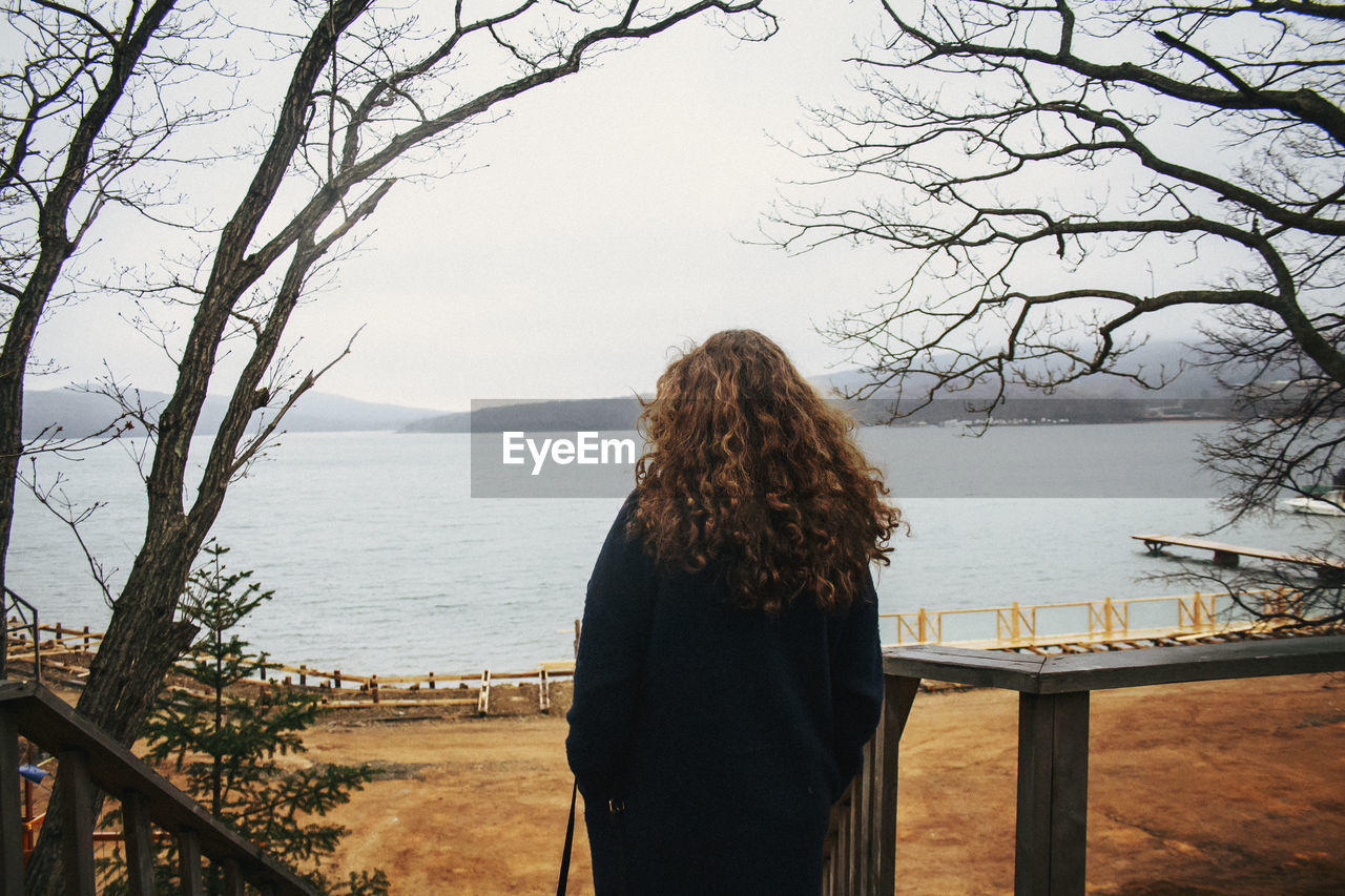Rear view of woman looking at lake against sky