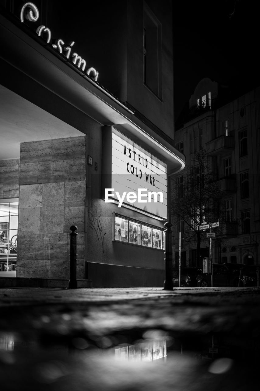 INFORMATION SIGN ON ILLUMINATED STREET AGAINST BUILDINGS IN CITY