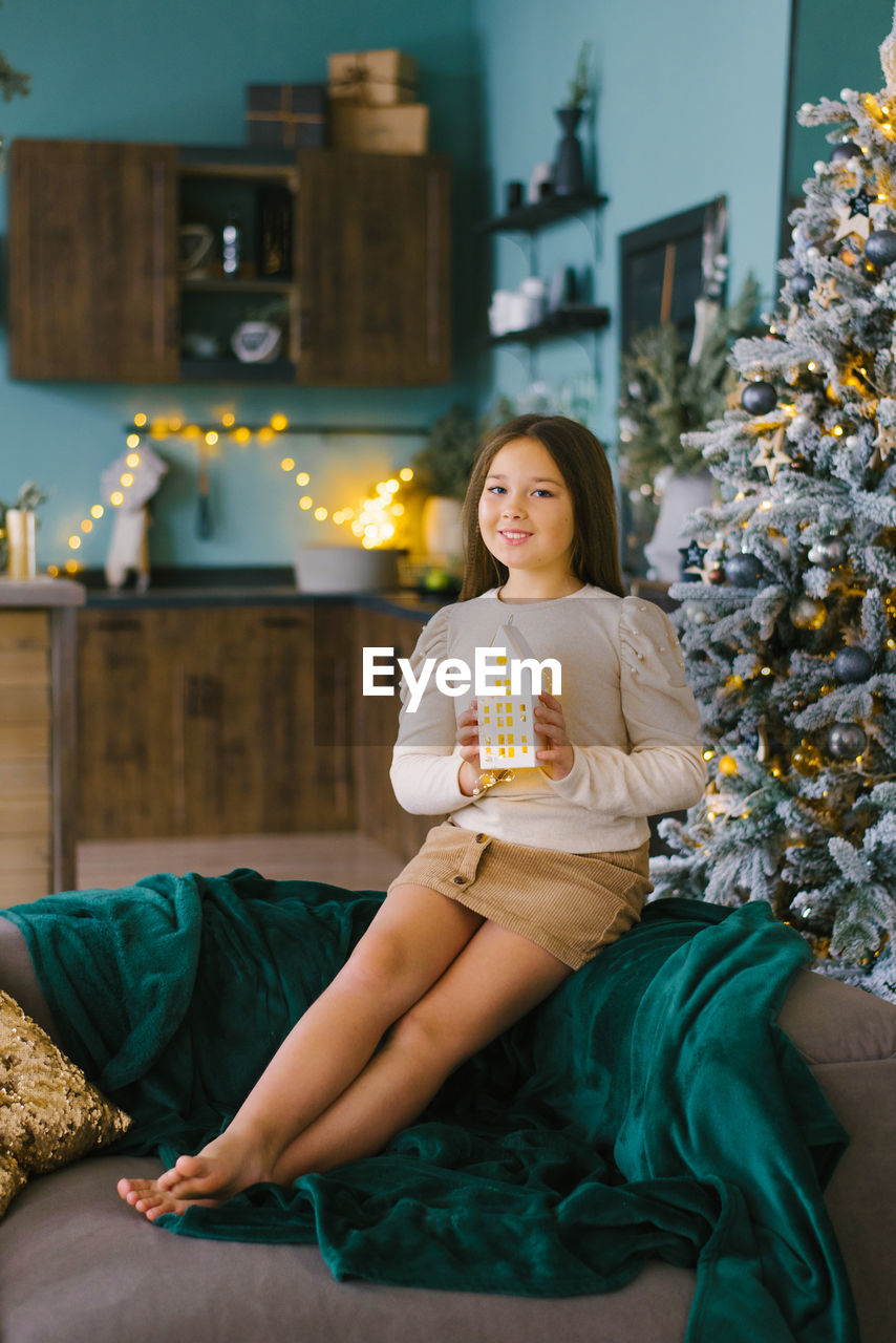 Cute girl holds a glowing toy house in her hands to decorate the house for christmas and new year