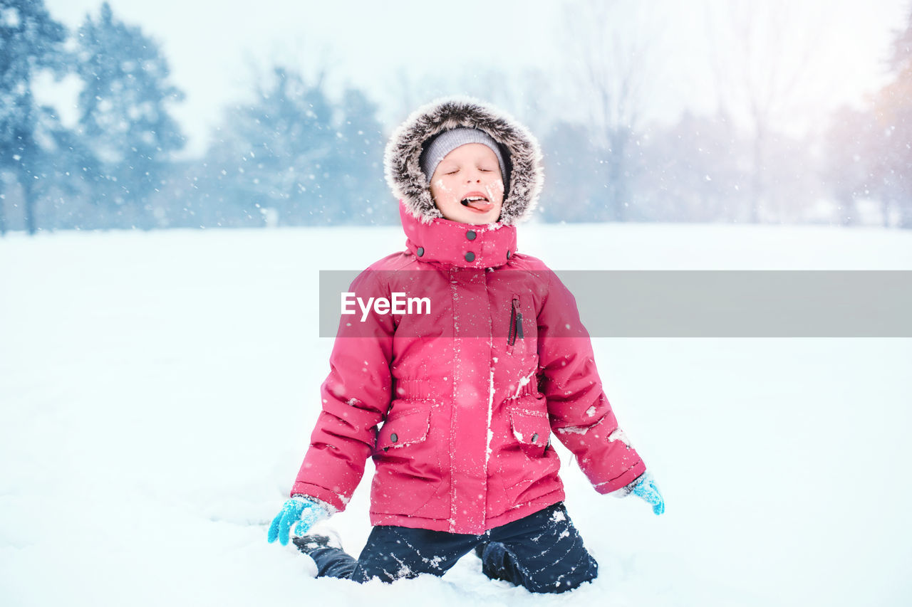 Girl kneeling on snow covered field during winter