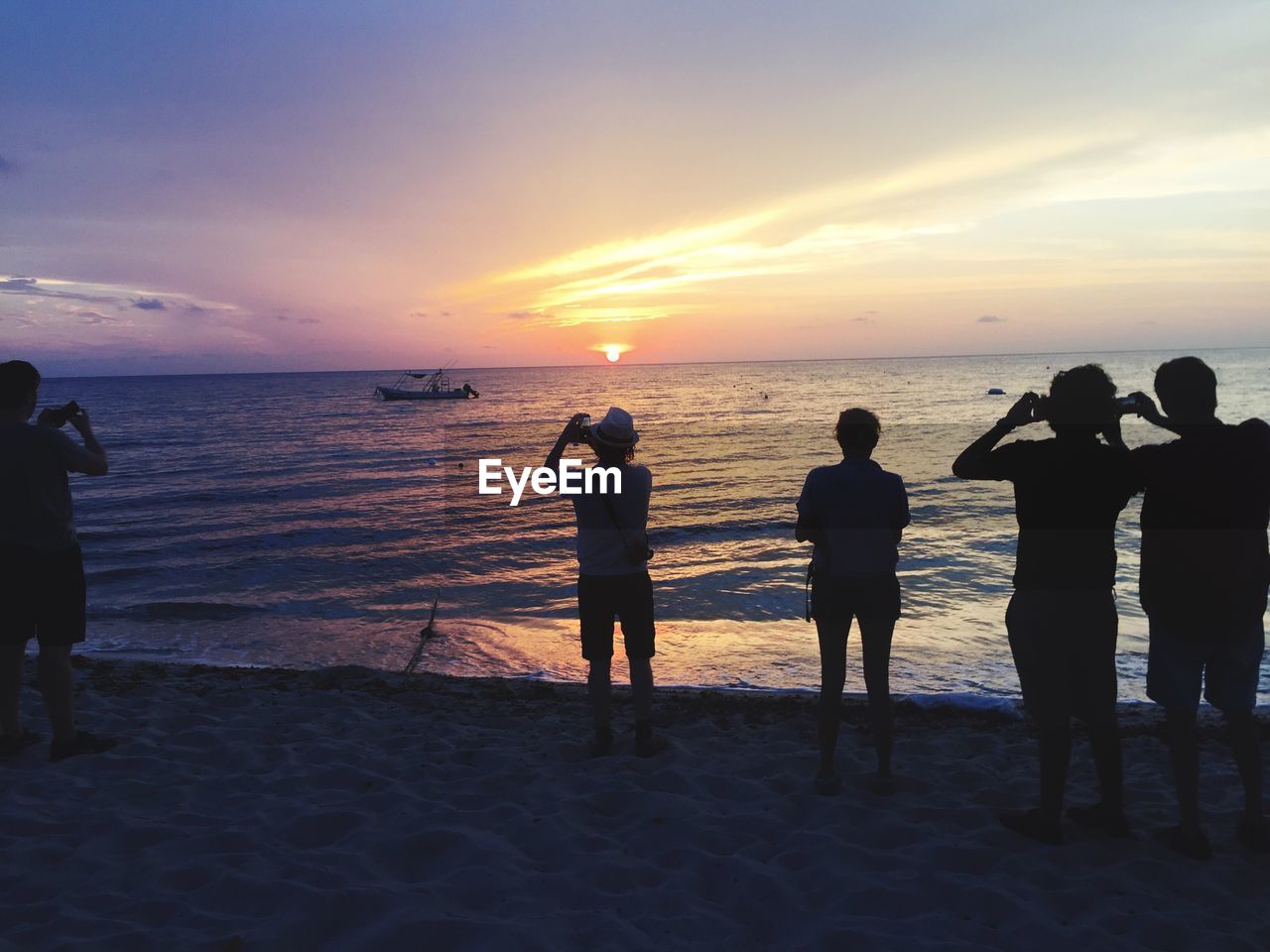 People standing on shore while photographing sunset over horizon