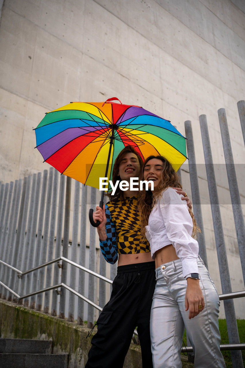 Young couple posing smiling under an umbrella with gay pride colors looking at camera. person