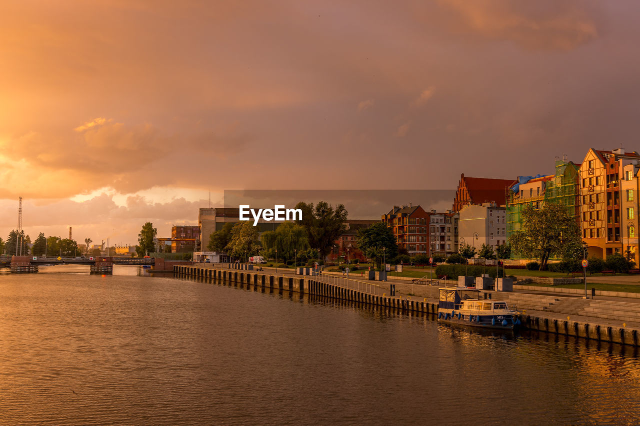 Bridge over river by buildings against sky during sunset