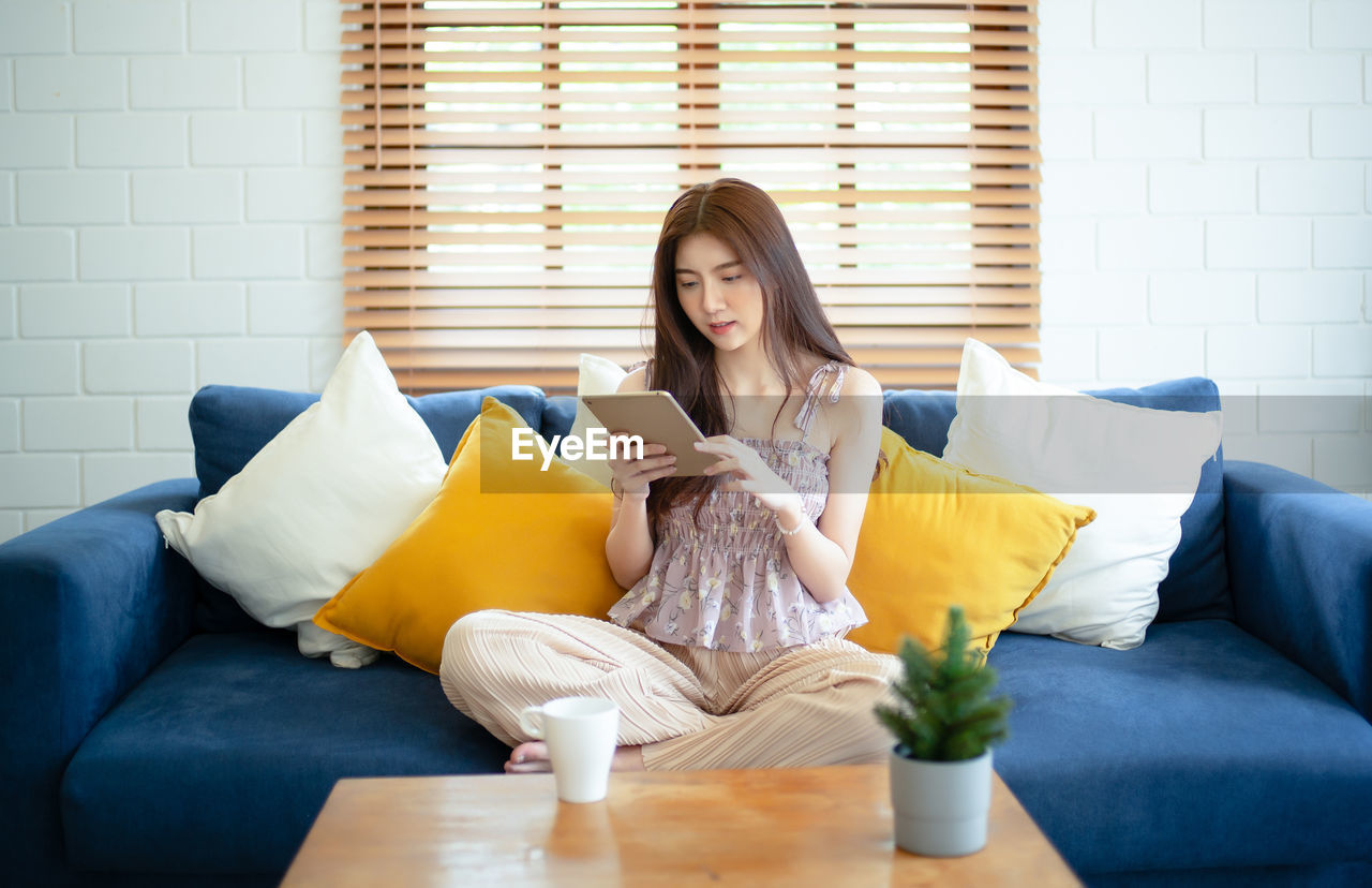 YOUNG WOMAN SITTING ON SOFA AT HOME