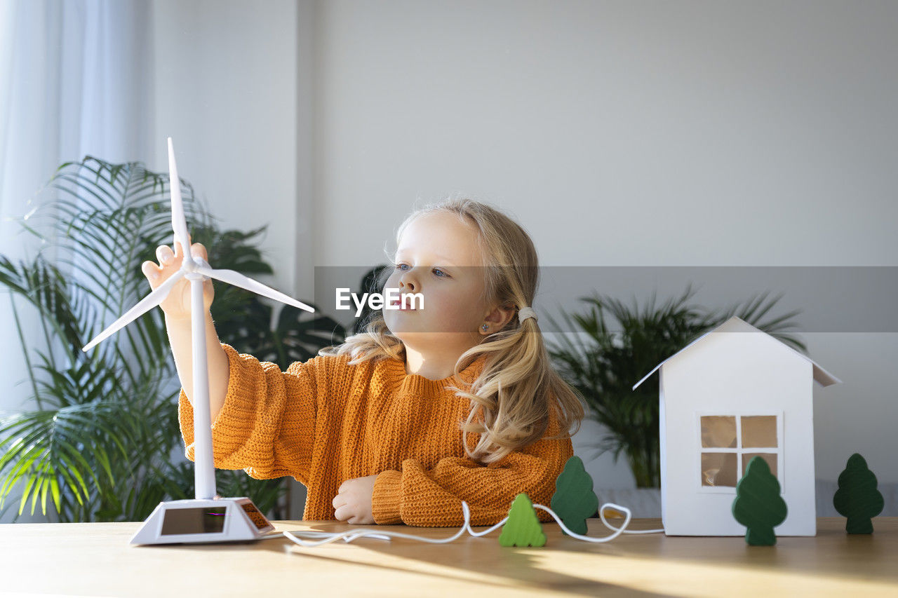 Girl holding wind turbine model at home