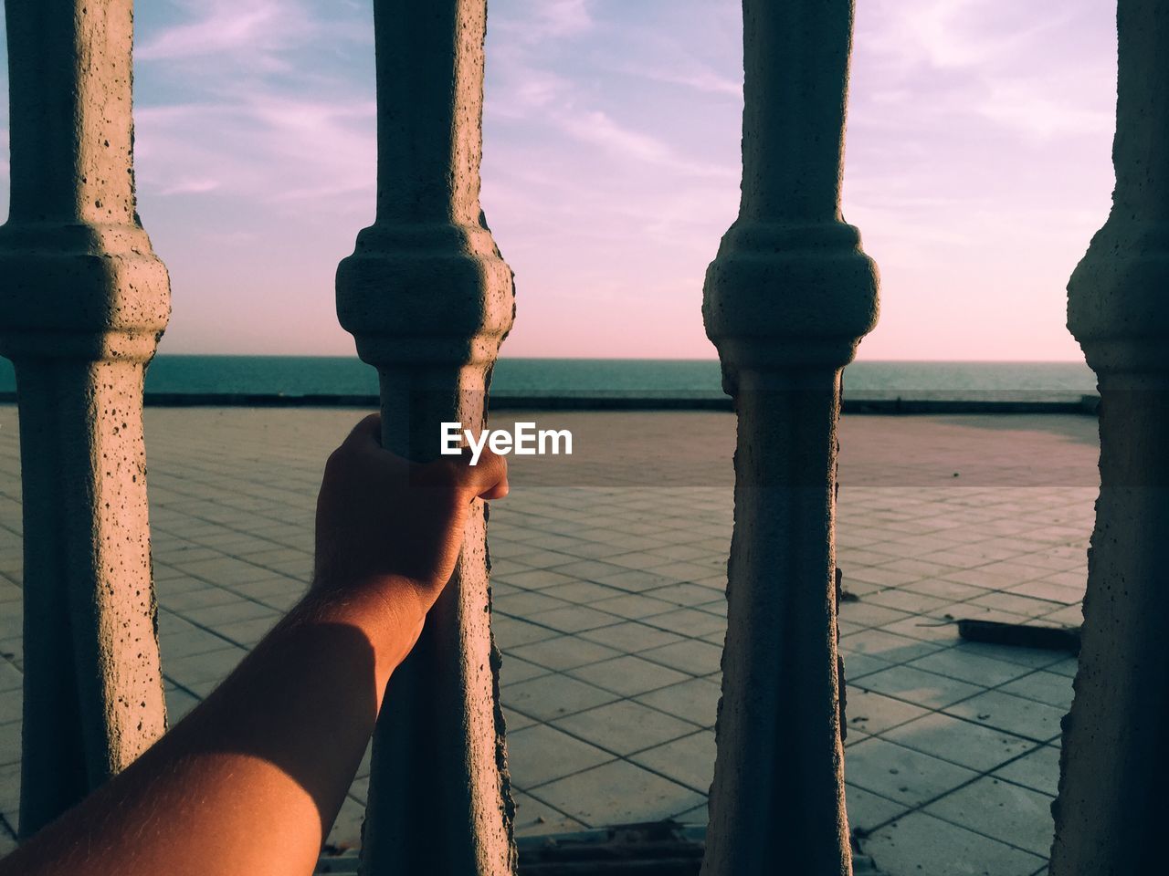Close-up of hand holding railing against sea at sunset