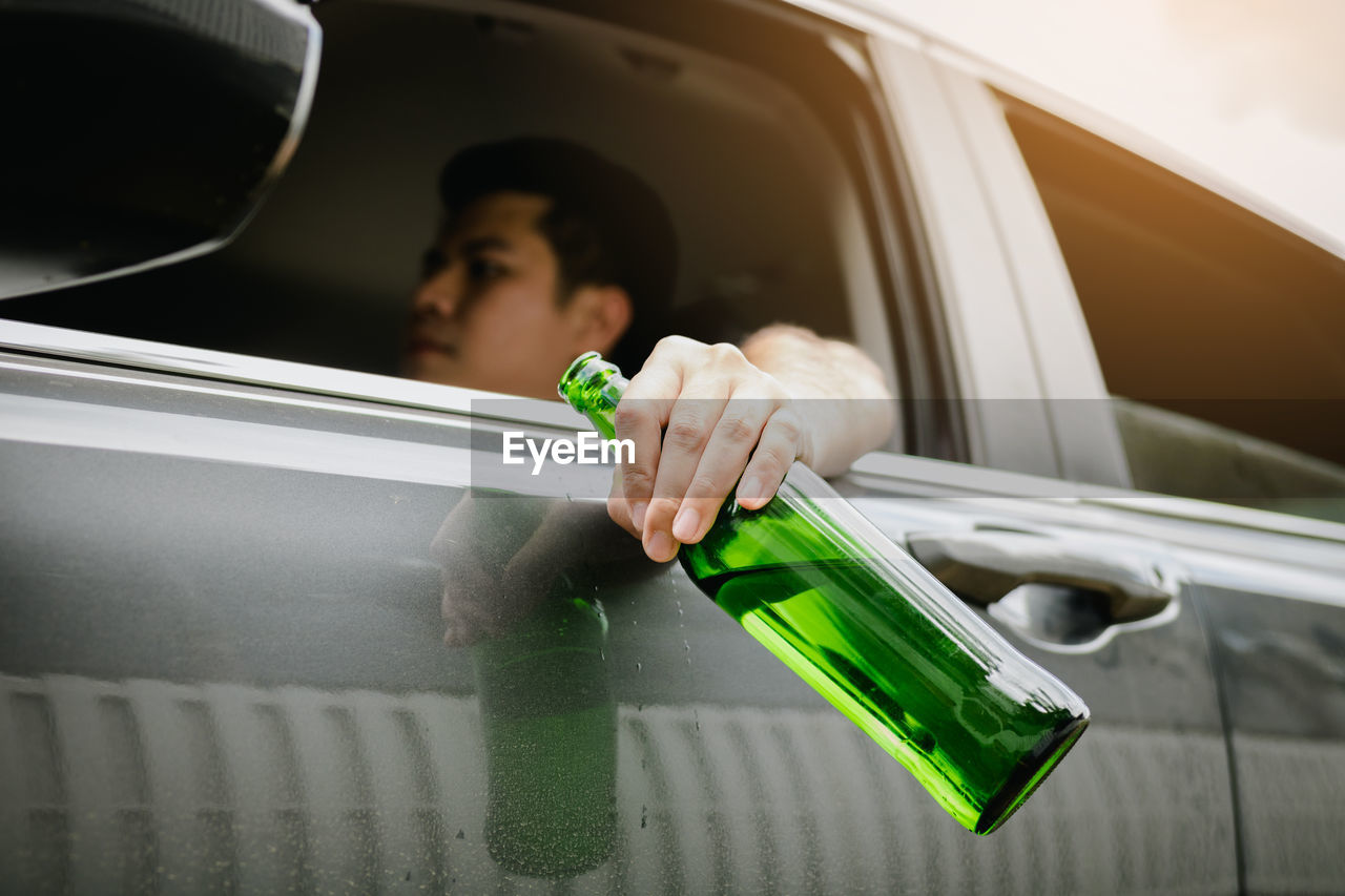 Man holding beer bottle while sitting in car