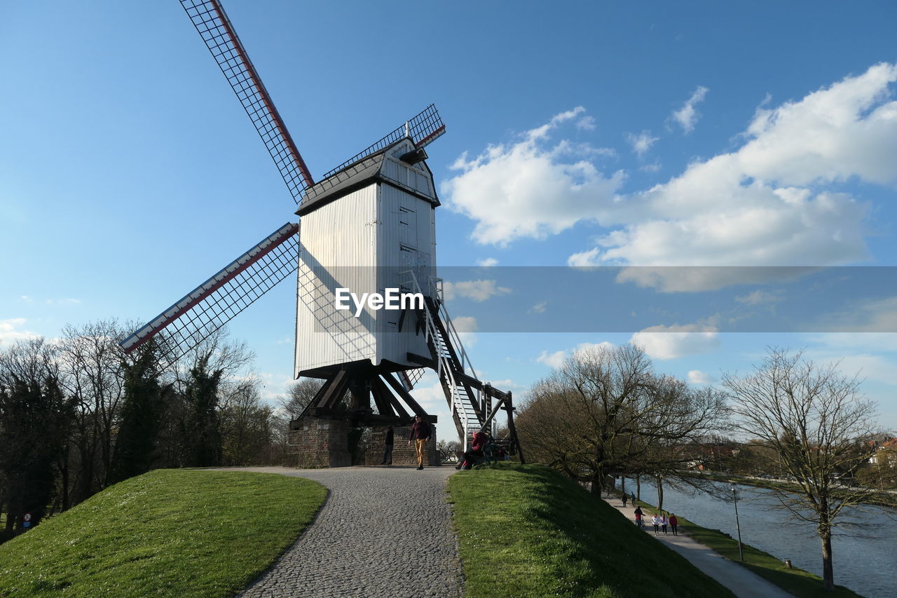 sky, windmill, renewable energy, environmental conservation, mill, alternative energy, nature, wind power, power generation, architecture, wind turbine, environment, turbine, cloud, plant, built structure, tree, traditional windmill, grass, day, no people, blue, wind, landscape, building, outdoors, water, rural scene, building exterior, travel destinations, technology