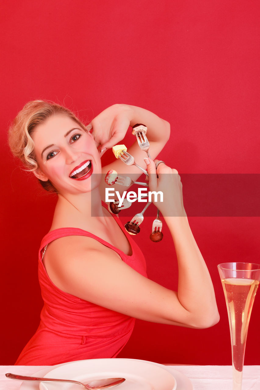 Portrait of smiling young woman having food and drink against red background