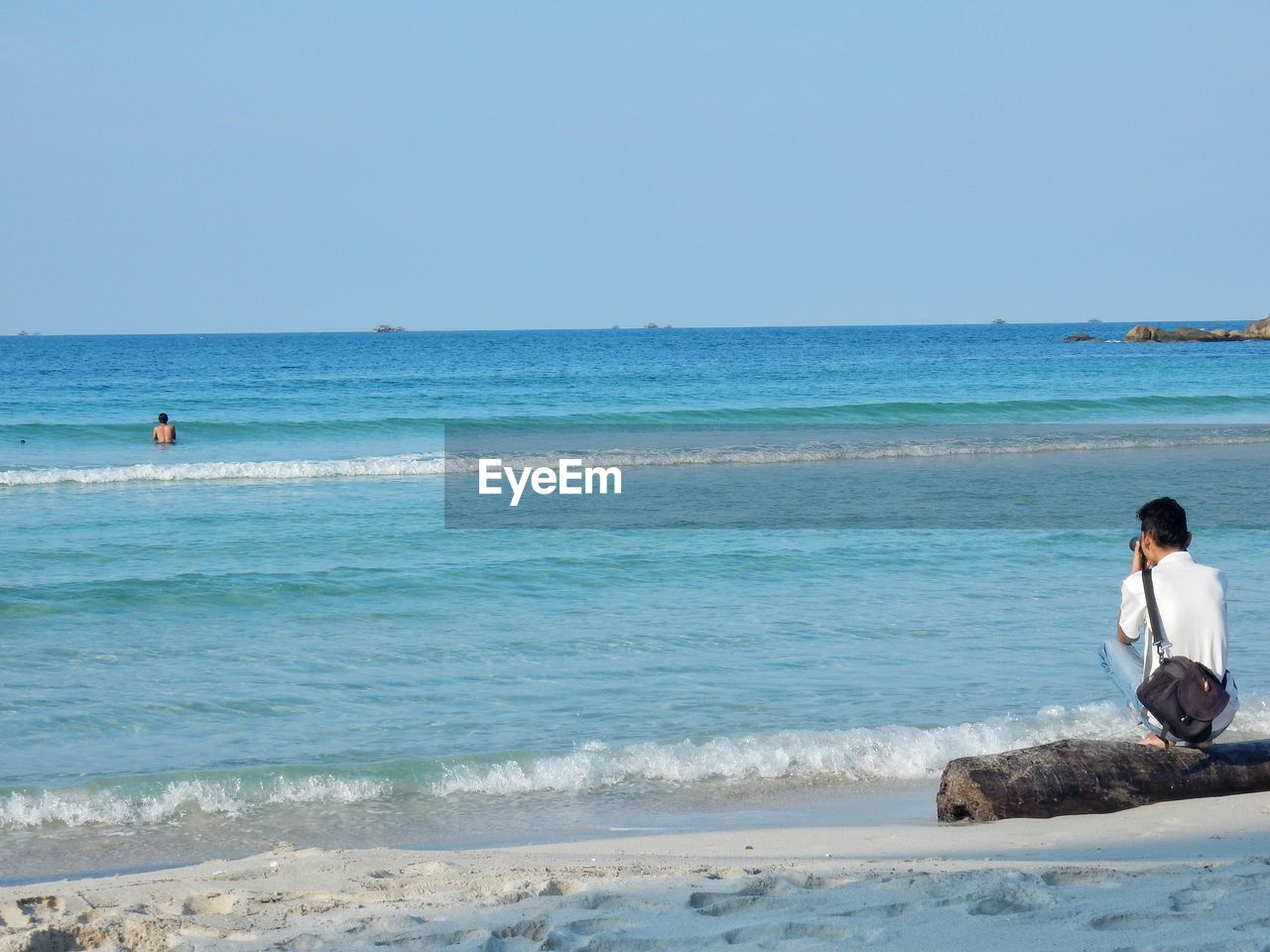 Rear view of photographer photographing man swimming in sea