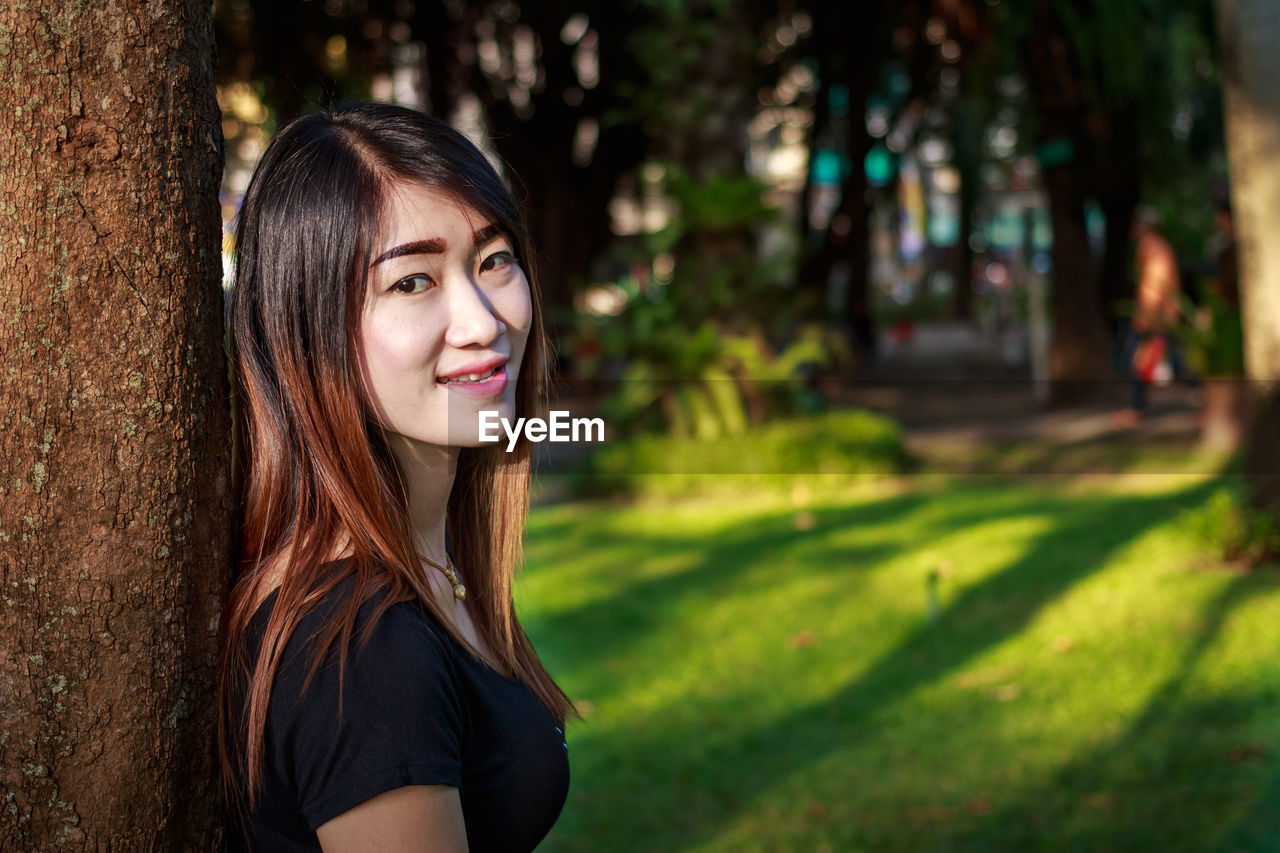 PORTRAIT OF SMILING YOUNG WOMAN WITH TREE