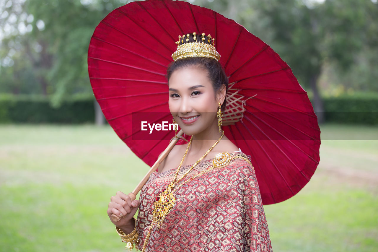 Portrait of a smiling woman holding umbrella while standing on field