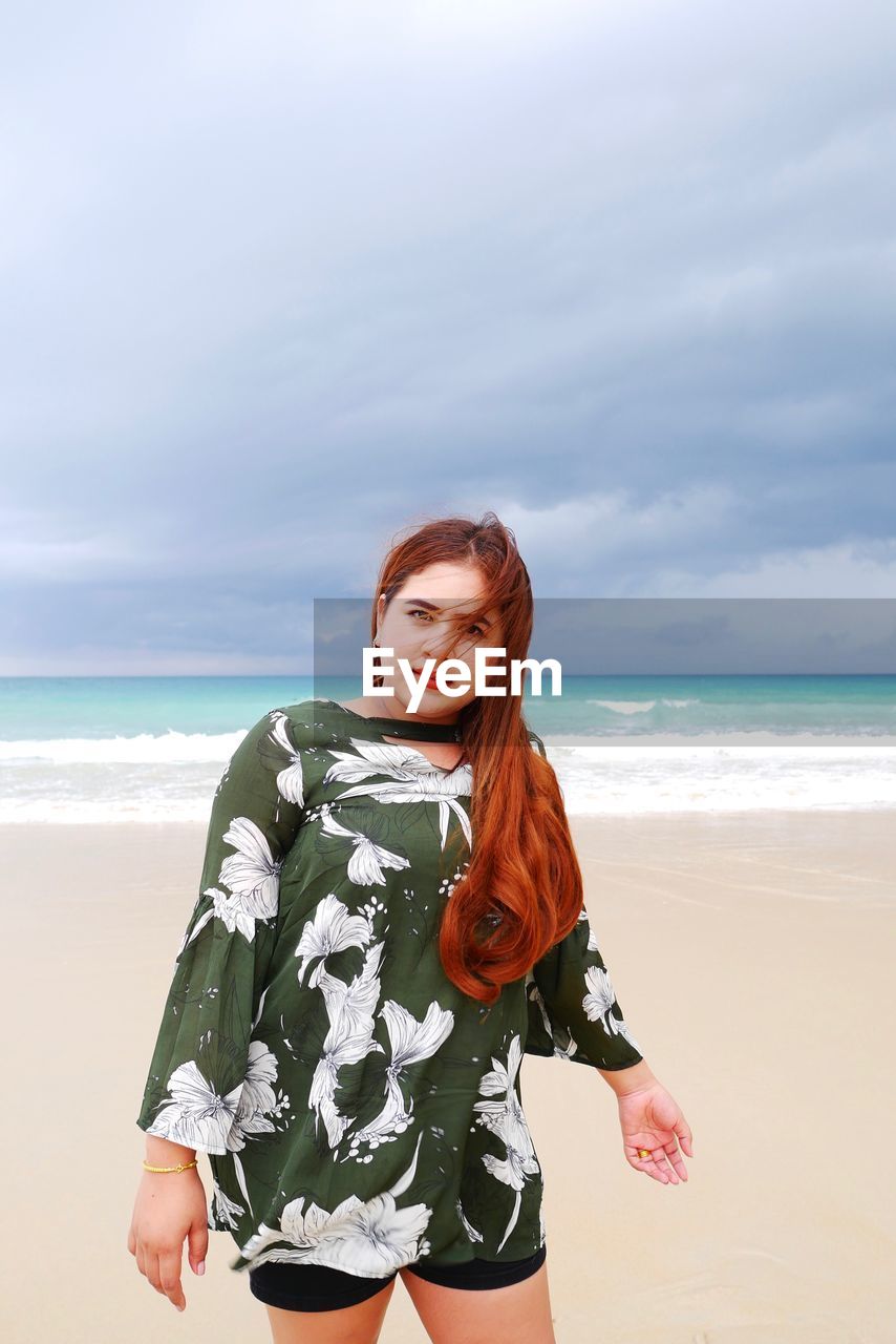 Young woman standing at beach against sky