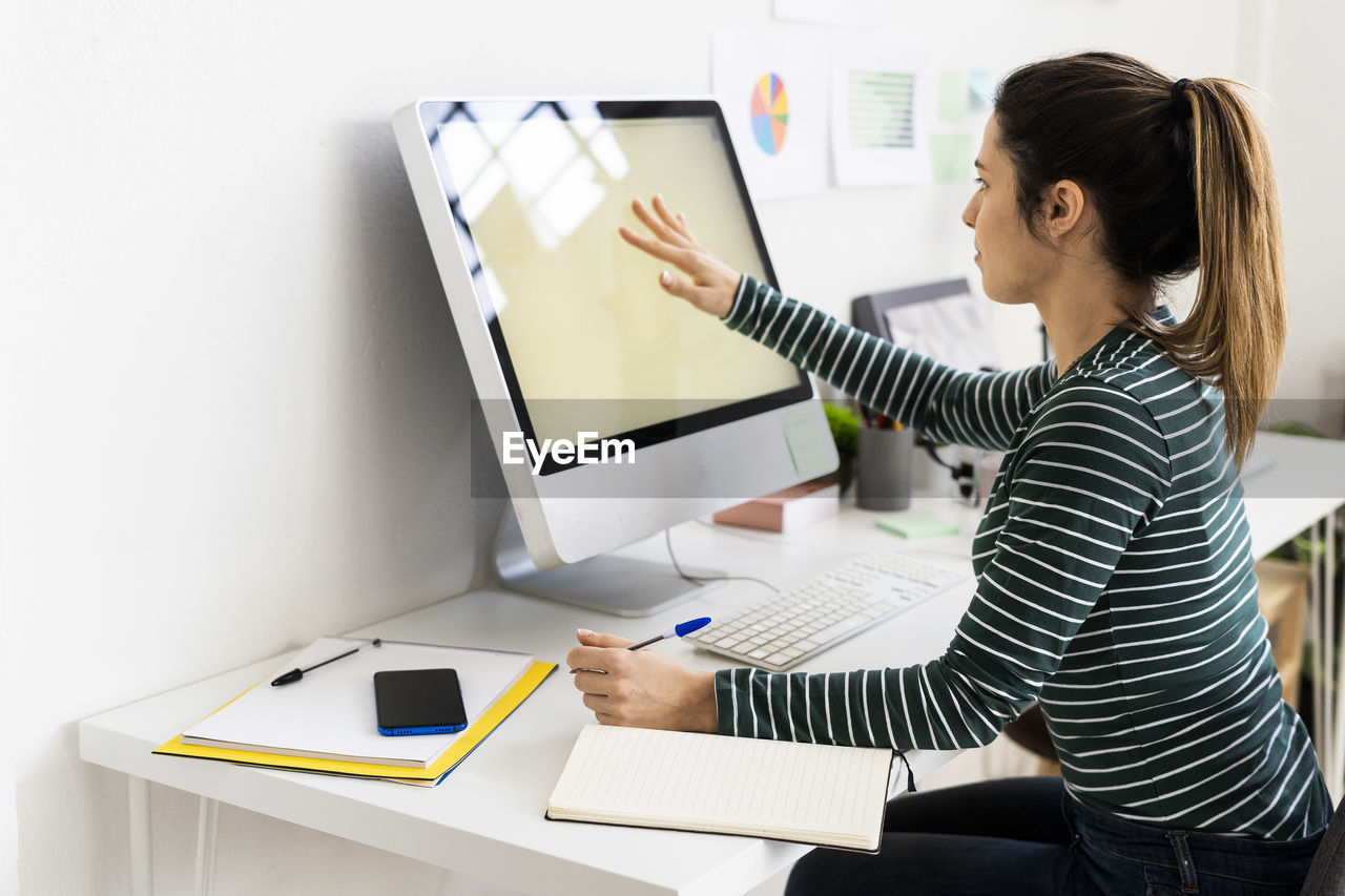 Creative businesswoman touching computer screen while working in office