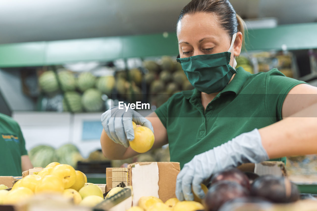 A woman wearing a mask placing fruit in the fruit shop