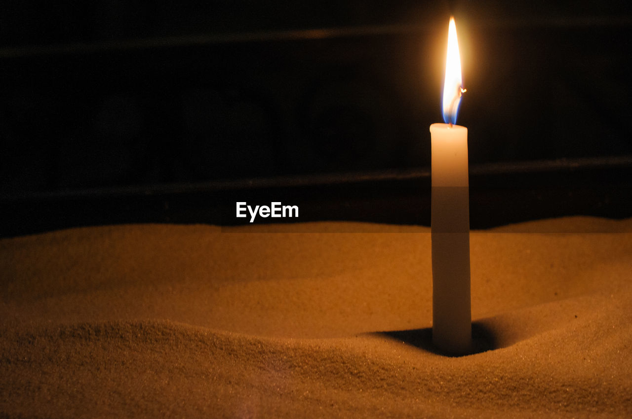 Close-up of illuminated candle on sand