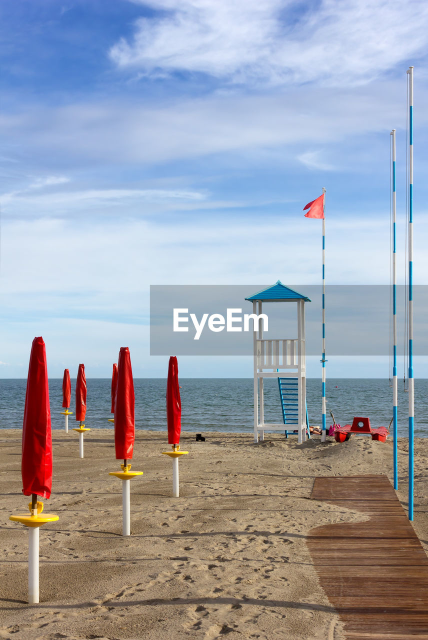 RED PARASOLS ON BEACH AGAINST SKY