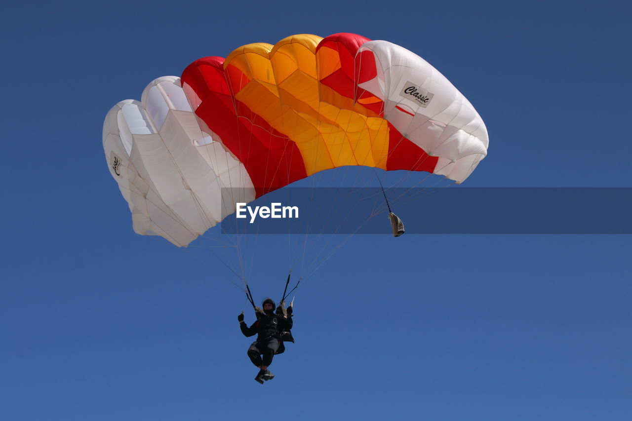 flying, extreme sports, paragliding, parachute, adventure, mid-air, sports, parachuting, sky, blue, joy, windsports, exhilaration, leisure activity, nature, motion, transportation, air sports, low angle view, gliding, sports equipment, one person, safety harness, warning sign, parasailing, skydiving, clear sky, risk, air vehicle, environment, pilot, day, sign, recreation, courage, full length, wind, multi colored, protection, outdoors, fun, activity, rope, lifestyles, positive emotion, emotion, wing, excitement