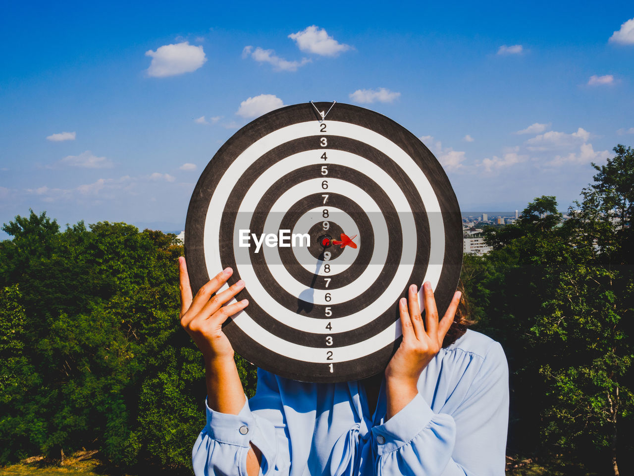 Woman covering face with dartboard against sky