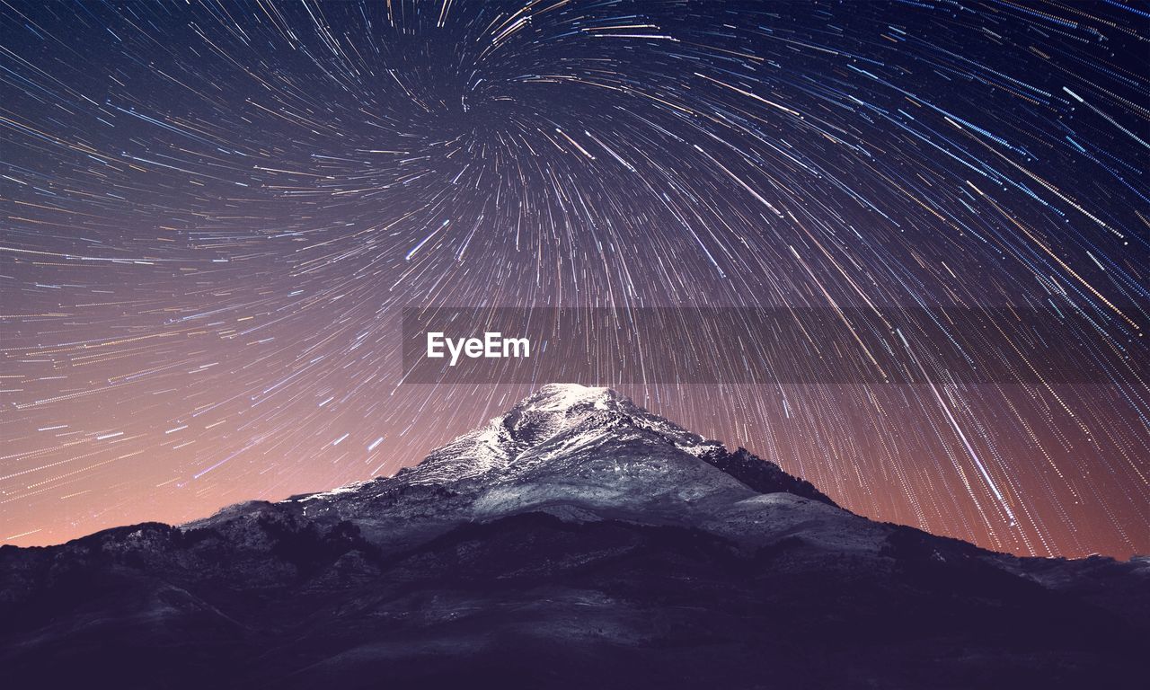 Low angle view of mountain against star trails against sky at night