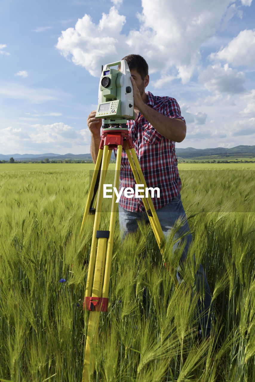 Engineer standing with equipment on field against sky