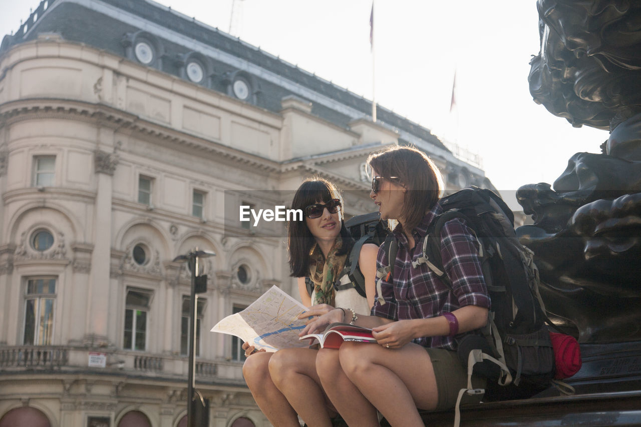 Female backpackers discussing over map while sitting at town square